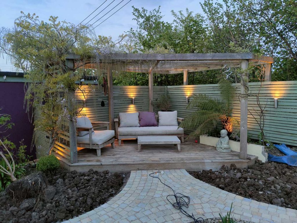 pretty triangular pergola in one corner of a garden lit with uplighters for a calm ambience