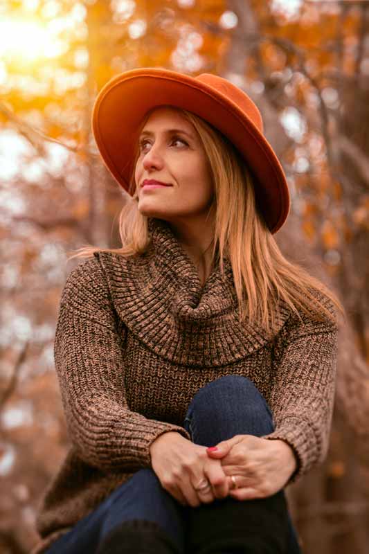 lady in warm winter jumper and red felt hat lifts her face to the sun