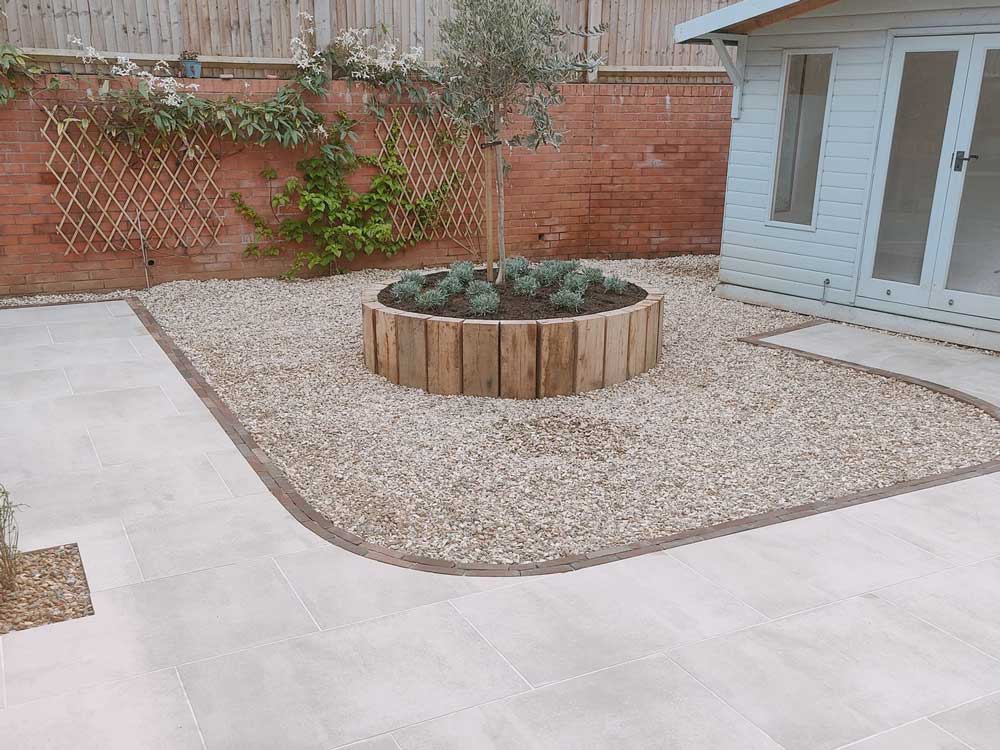 new build gardens without grass. Paved area with circular raised bed and pretty blue summerhouse