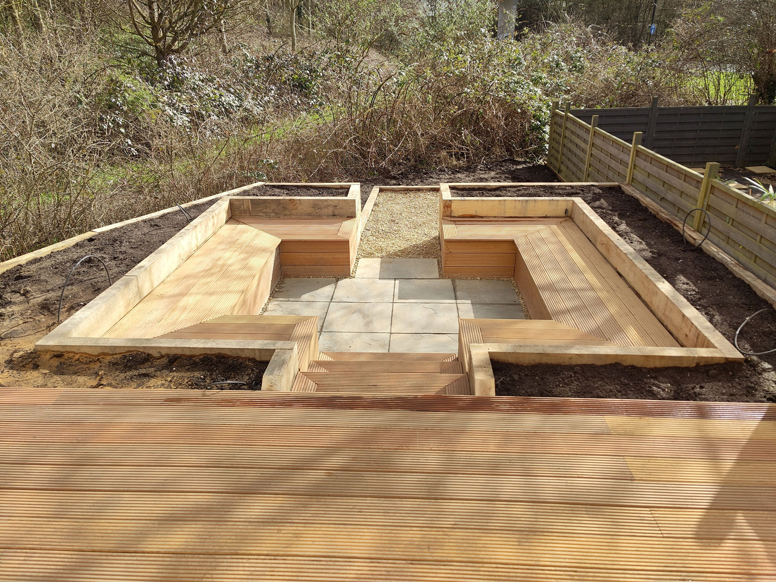 view from a large deck looking over a sunken patio enclosed by planting areas and timber benches
