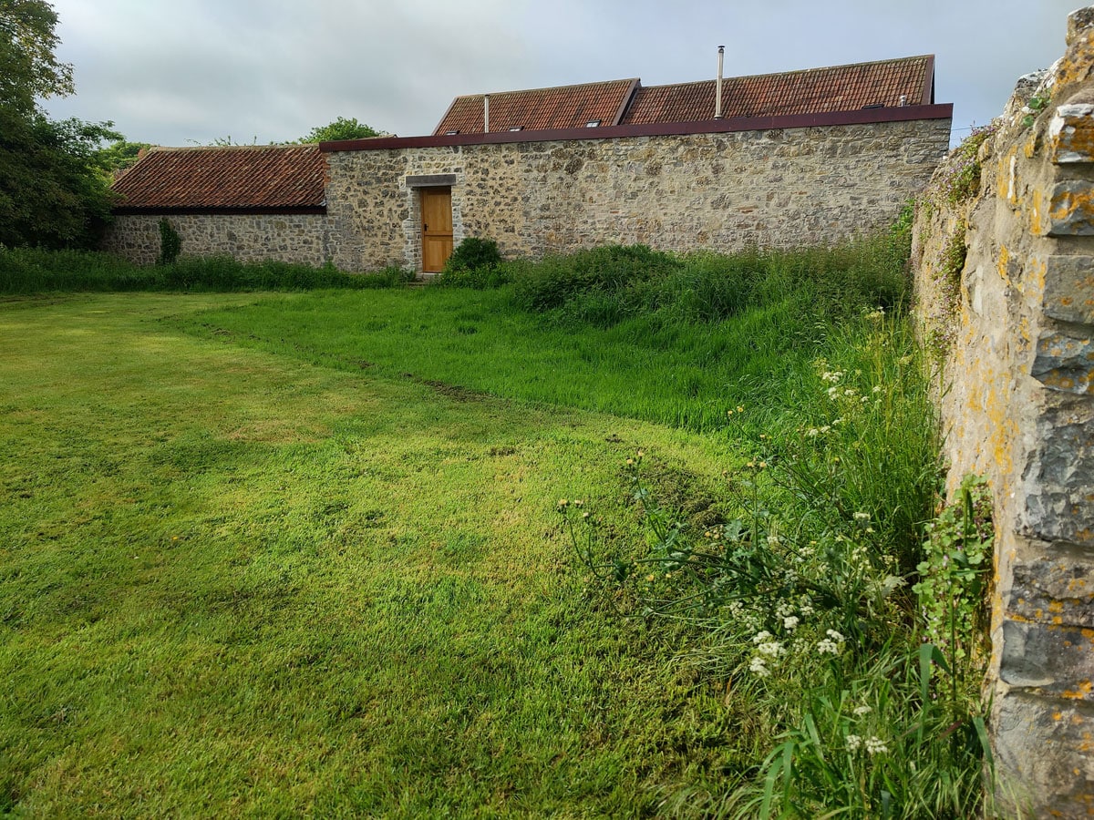 mown meadow with garden wall to right and barn beyond