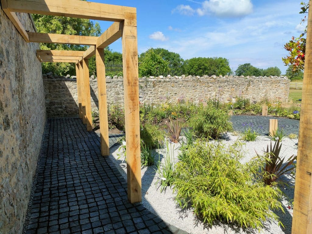 timber pergola adjoining an old stone wall to create shaded cloister