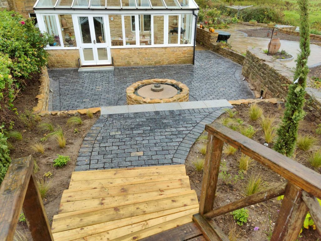 sloping garden with two terraces leading to cottage with conservatory